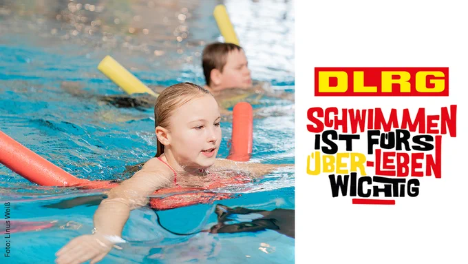 Ein Mädchen schwimmt mit Unterstützung einer sogenannten Schwimmnudel im Wasser. Es ist außerdem das Logo des Schwimmabzeichentags zu sehen. Darauf steht: "DLRG - Schwimmen ist fürs Überleben wichtig".