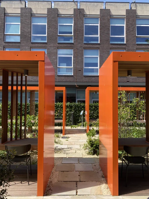 View of library garden shows greenery & blue skies contrasted with orange seating frames