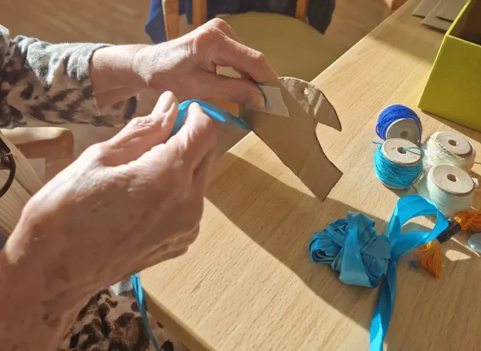 A pair of hands, holding cardboard. Some ribbon and cotton reels on a table.