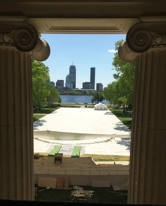 View of Killian Court seen through two pillars. Workers setting up a large white tent for commencement.