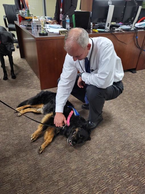 Washington Dulles VP and Airport Manager Richard Golinowski petting a black therapy dog that is lying down on the floor of the Airport Manager's office