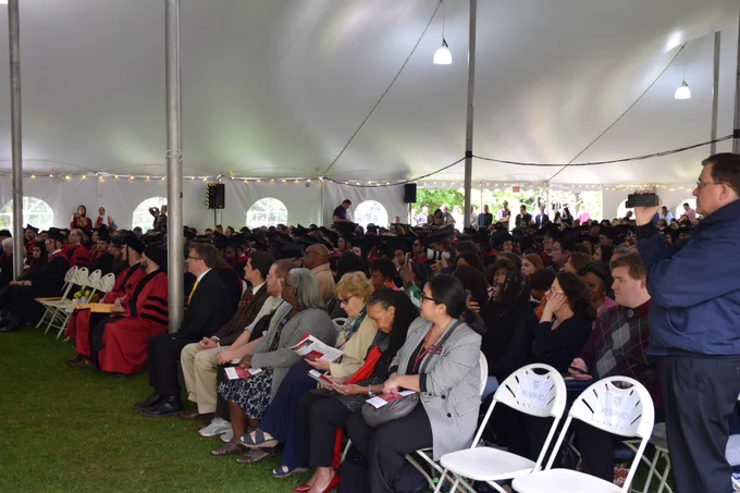 Family and students sit beneath a white tent listening to Dean Hempton address the graduating class.