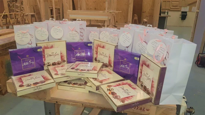 13 boxes of chocolates on a table with 19 gift bags in a joinery workshop