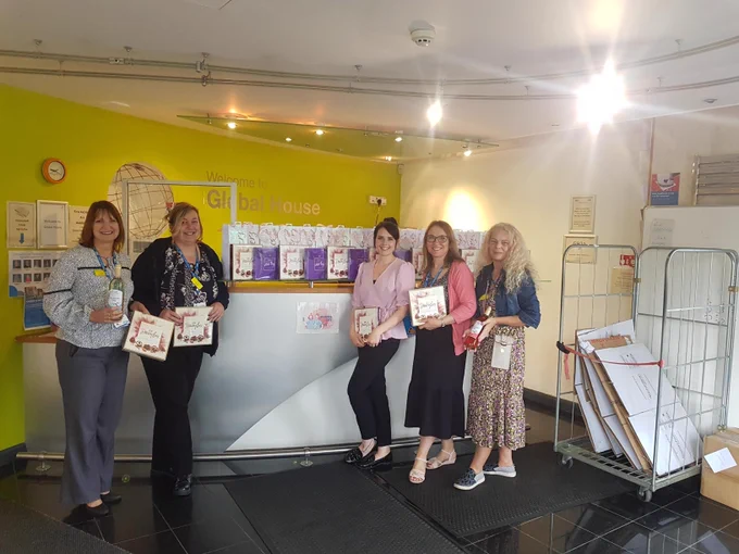 Four female ladies stood in a row holding boxes of chocolates and smiling.