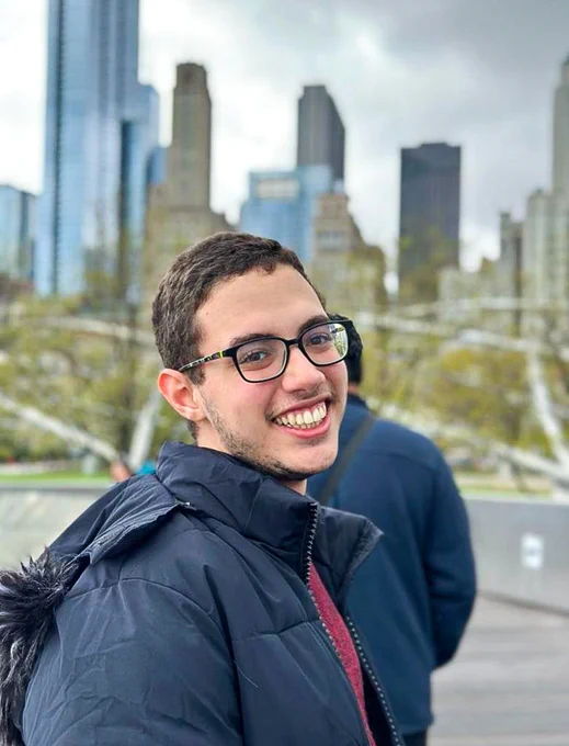 Aymane Bouhazzama smiles in front of a city skyline.