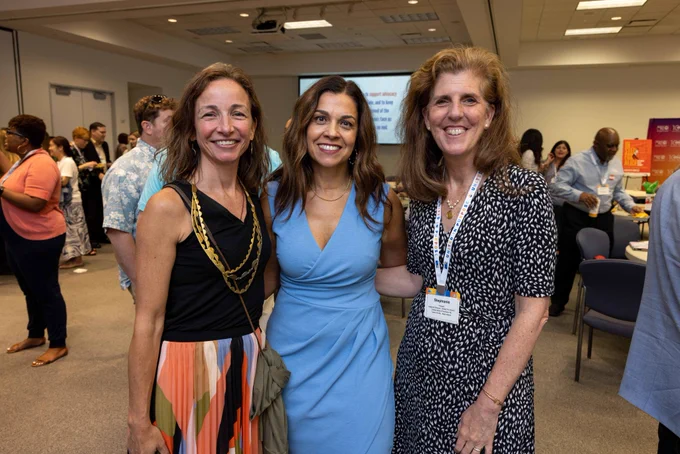 Kiran Handa Gaudioso stands in the middle, with Stephanie Hoopes on the right and an event attendee on the left. Dressed in casual business attire, all three smile at the camera.