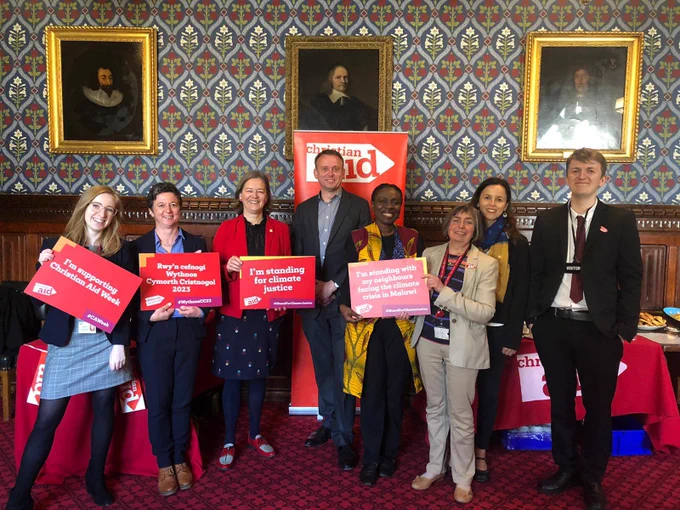 A group of Christian Aid staff standing in a row in front of a Christian Aid banner in a House of Commons room