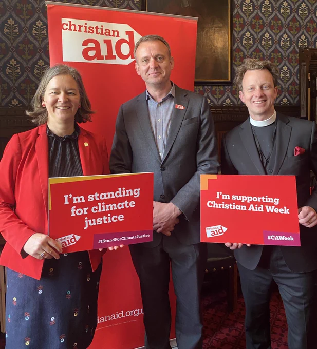 Fleur, Christian Aid CEO Patrick Watt, and Rev Brutus Green holding signs saying I’m standing for climate justice and I’m supporting Christian Aid Week