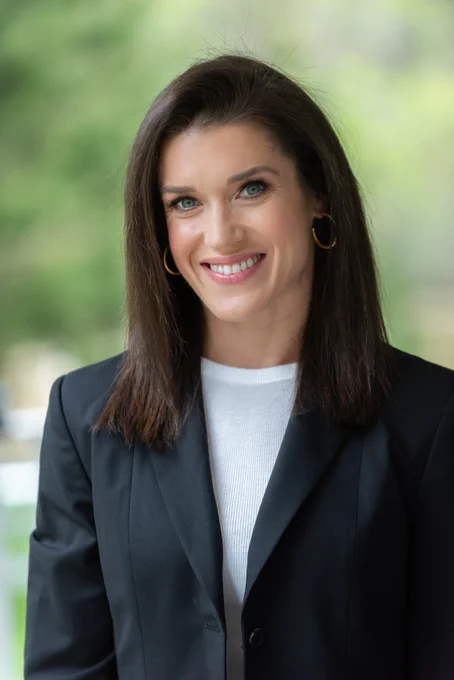 Rebecca Alexander, a woman with shoulder length dark brown hair, is wearing a white blouse under a black blazer