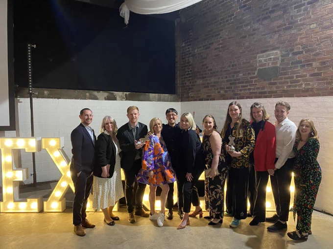 A group of people stand in front of large lit-up letters which spelt he word EXPOSED. 