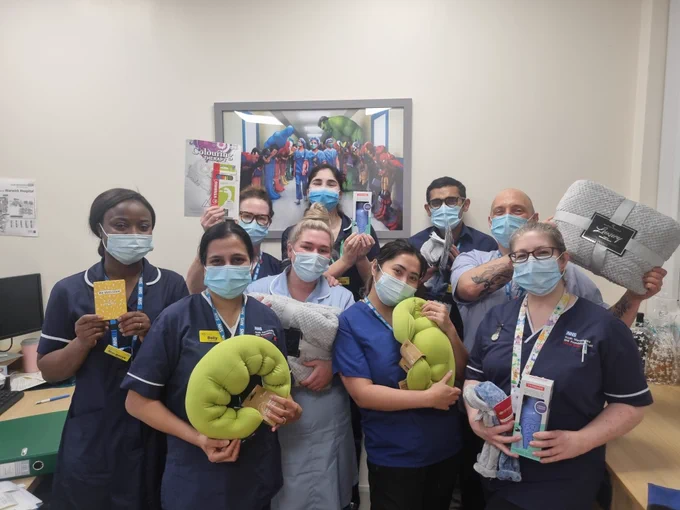 A group of nurses holds items from a chemotherapy care pack, including a blanket, neck pillows and colouring books