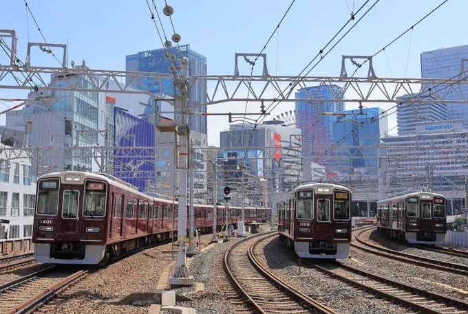 Image description: Image of Hankyu railway station. Three trains with multiple rail tracks surrounding them. There are buildings in the background