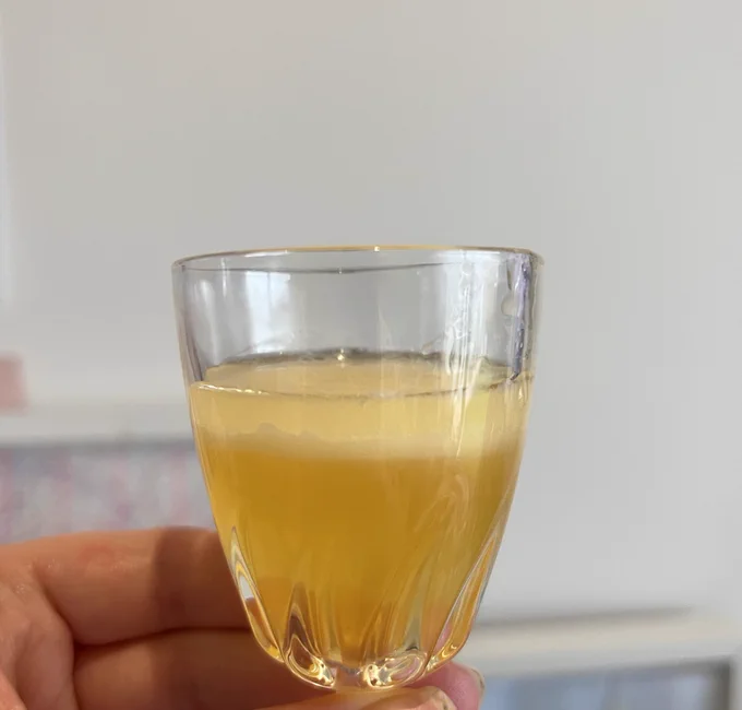 A small glass filled with pale yellow liquid, most of the liquid is transparent but there is a thin creamy yellow layer on the top.