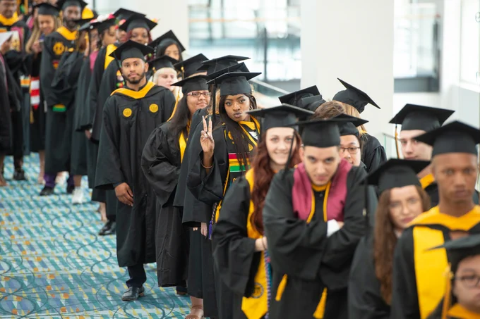 Students in caps and gowns line up to receive their diplomas at graduation.
