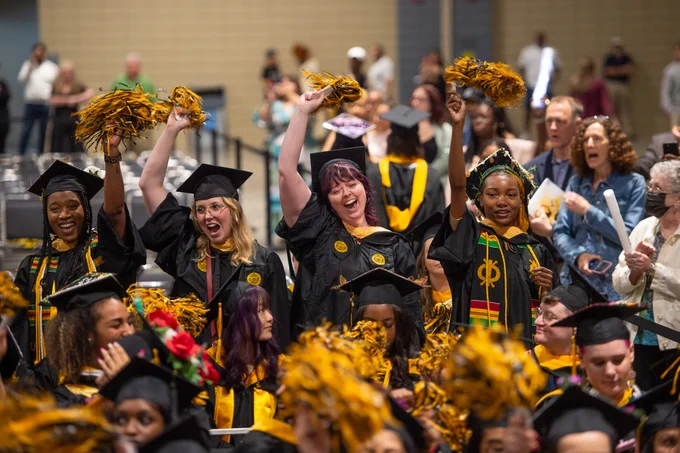 VCU graduates in caps, gowns, and cords wave black and yellow pom poms.