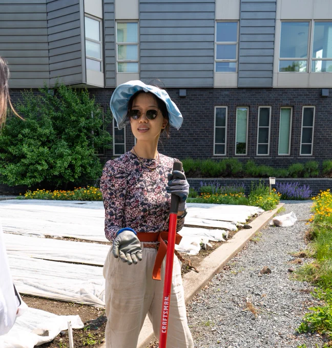 Althea standing and talking to someone while holding a red shovel in her left hand.