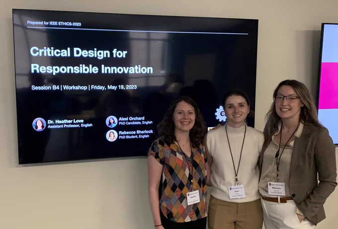 Three researchers stand in front of presentation screen in classroom