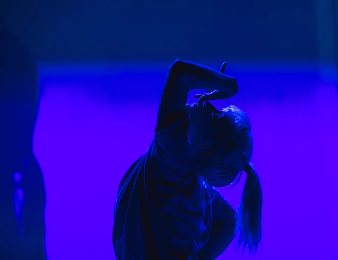 PRODUCTION SHOT, Alice blue lit with her head bent backwards and her arm / hand stretched over her face