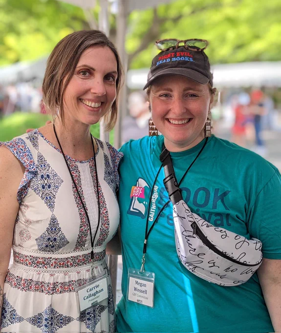 Me, a white woman with brown hair, in a white and blue dress standing with @abookishaffair, a white woman with a cute smile, who is wearing a green Gaithersburg Book Festival T-shirt