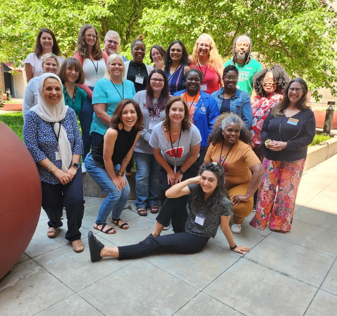 A diverse group of 21 ECS facilitators and staff posing for a photo in a courtyard with trees behind them