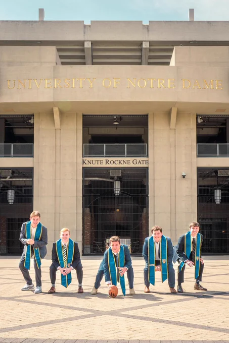 Five seniors pose like the offensive line in front of the Knute Rockne Gate at the football stadium.