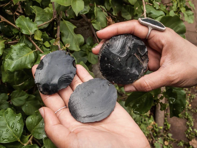 Hand holding three circular pieces of obsidian
