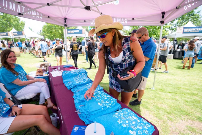 A woman grabbing a KAMU t-shirt from KAMU booth.