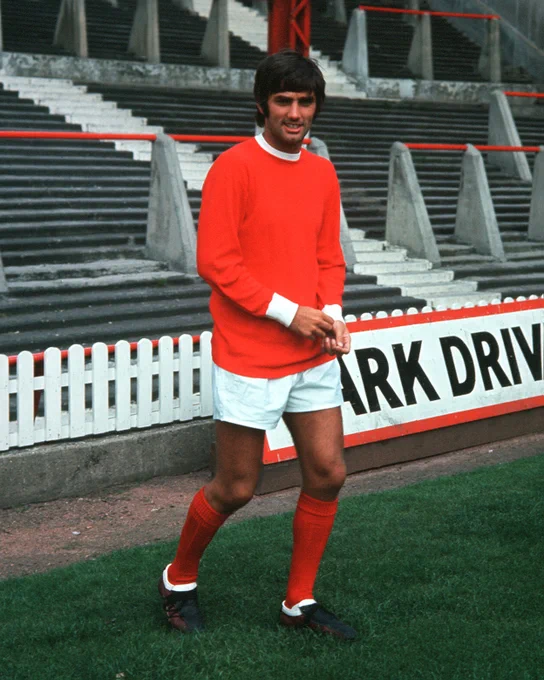 Colour photo of George Best, wearing a United home strip of red shirt with white collar and cuffs, white shorts and red socks.