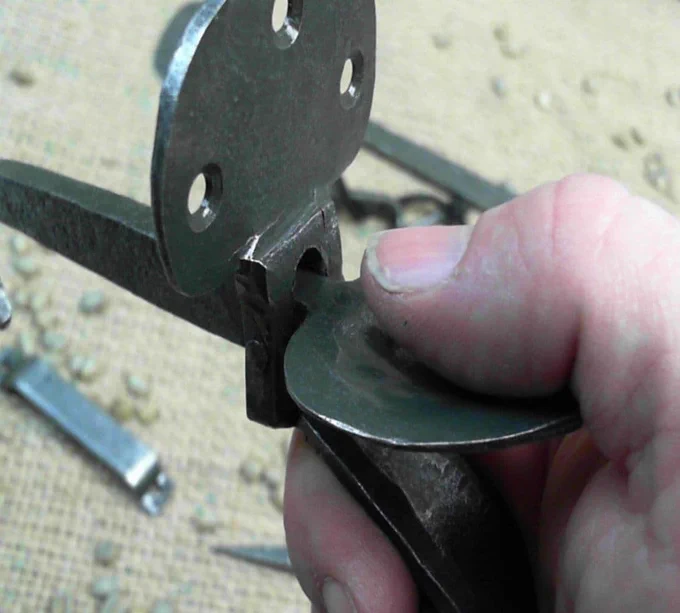 Thumb pushing down on a flat piece of circular metal, at the top part of a door latch.