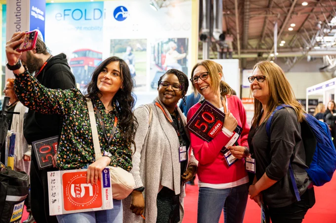 4 visitors taking a selfie at Naidex smiling with their show guides 