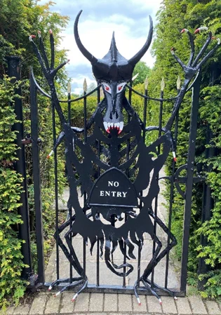 A photo of a spiky iron gate featuring a demonic figure and a sign that reads 'No Entry'. 