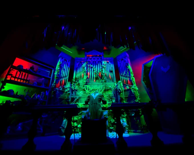 The organist inside Vampire's ride station with atmospheric spooky lighting and an eerily opened coffin beside.