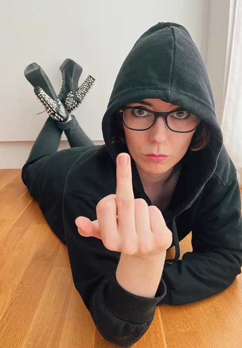 Pind lying on the floor in a black hoodie giving the finger to the patriarchy while staring intensely into the camera.