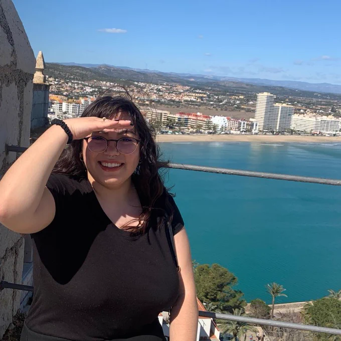 Litzy atop an overlook with the ocean and a city in the background.