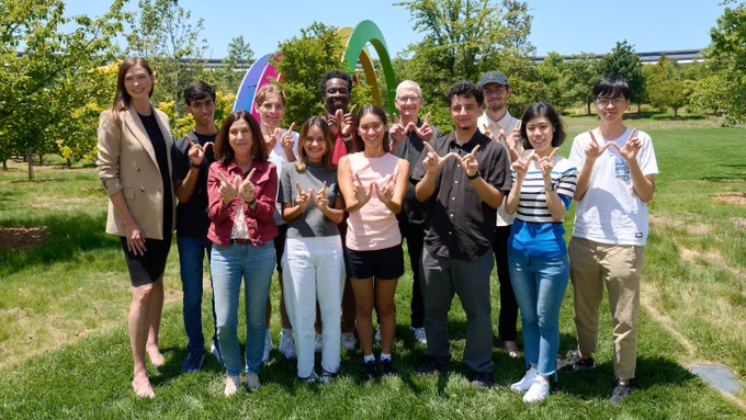 Tim, Susan Prescott, and Karlie Kloss stand with Swift Student Challenge winners near the rainbow at Apple Park.