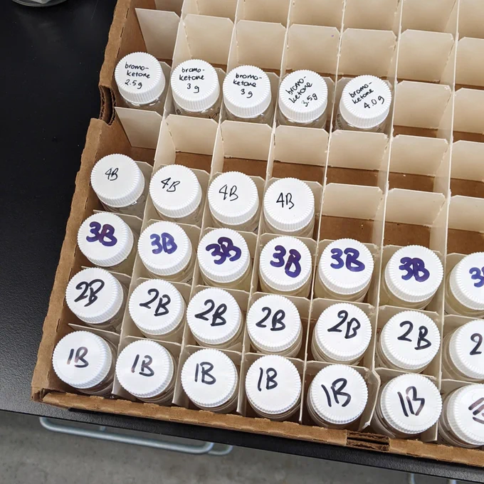 A 10 X 10 vial holder containing about 2 dozen vials with labels of 1B, 2B, 3B, 4B and bromoketone. 