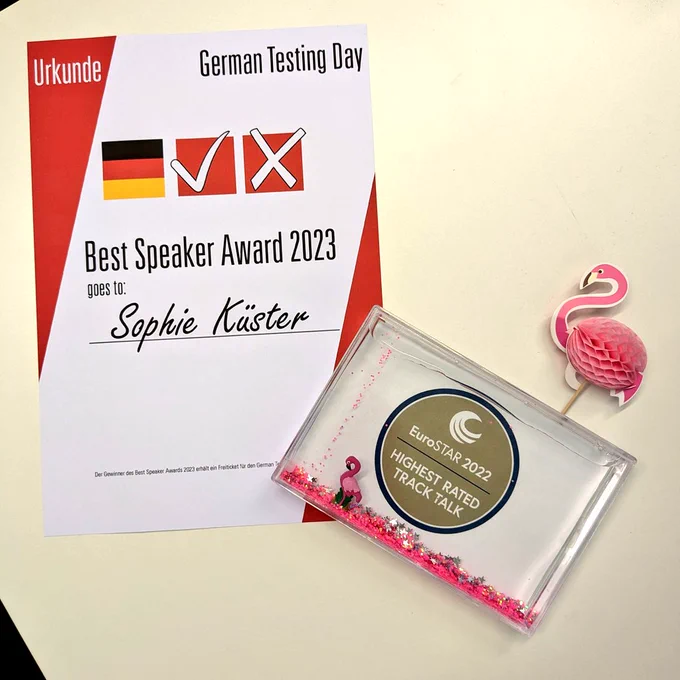 My certificate for Best Speaker Award at German Testing Day 2023 and for Highest Rated Track Talk at EuroStar 2022 lying on my office desk. The one from EuroStar is in a frame that doubles as a snow globe with pink glitter and a little floating flamingo 