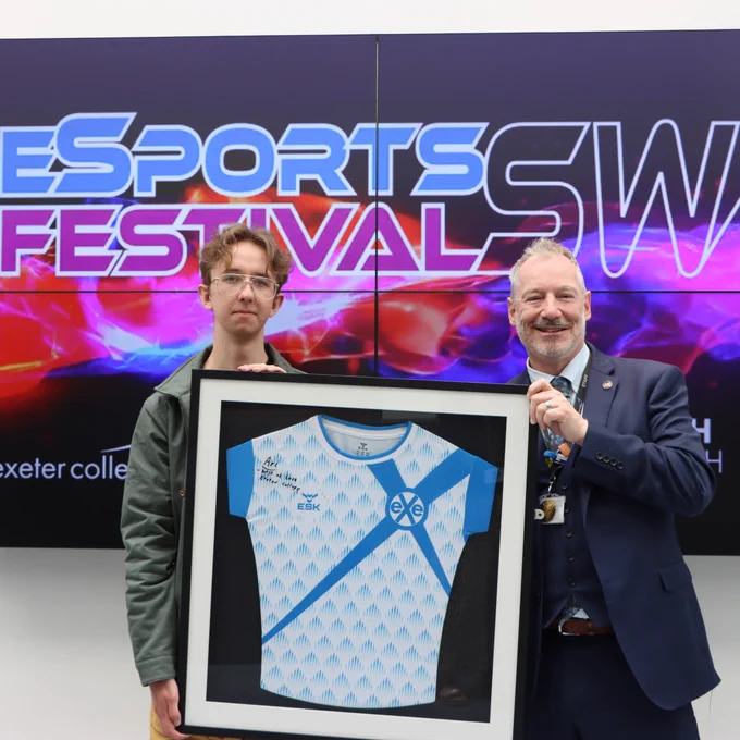 Principal of Exeter College, John Laramy, stands with pro esports layer Matt Walker. They're holding an Exe Esports Academy shirt that has been signed by Matt. 