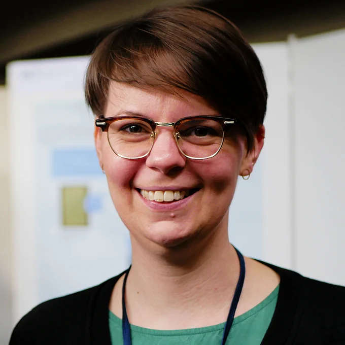 photograph taken at the DHd conference 2020 in Potsdam, showing Hannah Busch (woman with short hair and glasses) smiling at the camera in front of poster presentations in the blurred background