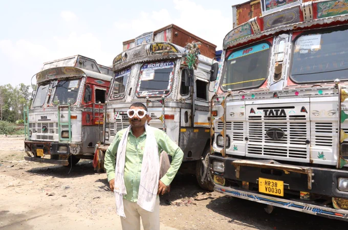 A man stands in front of a bus, wearing heart-shaped glasses. He smiles at the camera. 