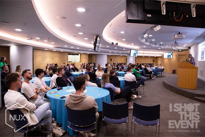 The audience at NUX manchester sat around tables facing the stage whilst Gareth presents his talk