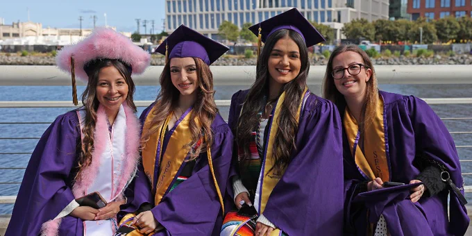Four graduates pose for a photo by the portwalk at Oracle Park at SF State Commencement
