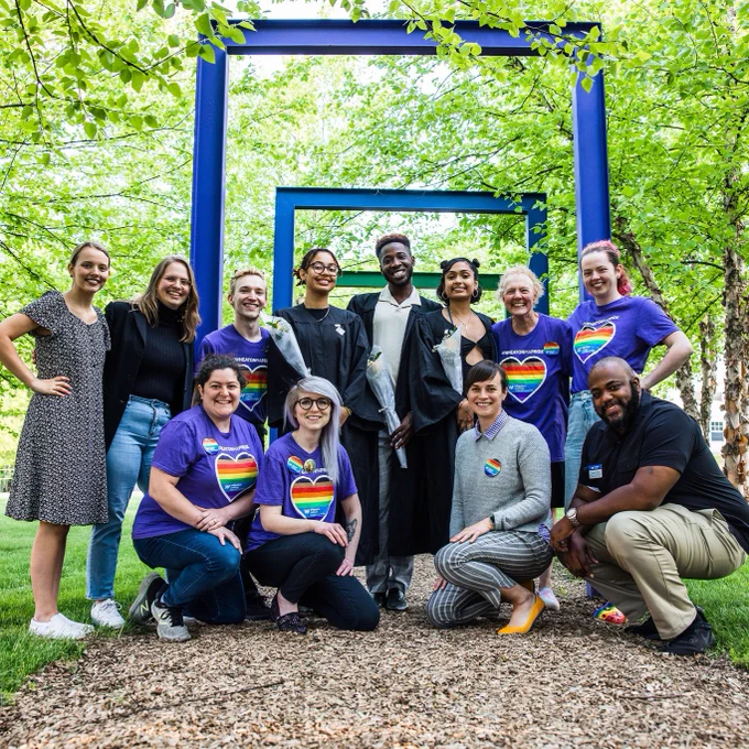 Students, faculty and staff pose for a group photo under the rainbow arches following Lavender Graduation.