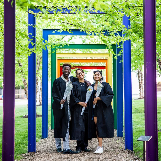 Three students smile and pose for a photo under the rainbow arches.