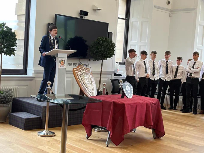 Provost Xander McDade standing on a stage beside two shield trophies