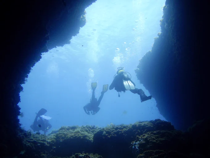 Scuba divers swimming through an underwater tunnel