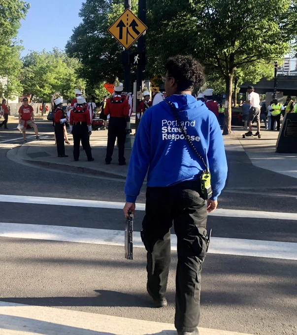 A Portland Street Response employee in a logo-ed sweatshirt walks the parade route.