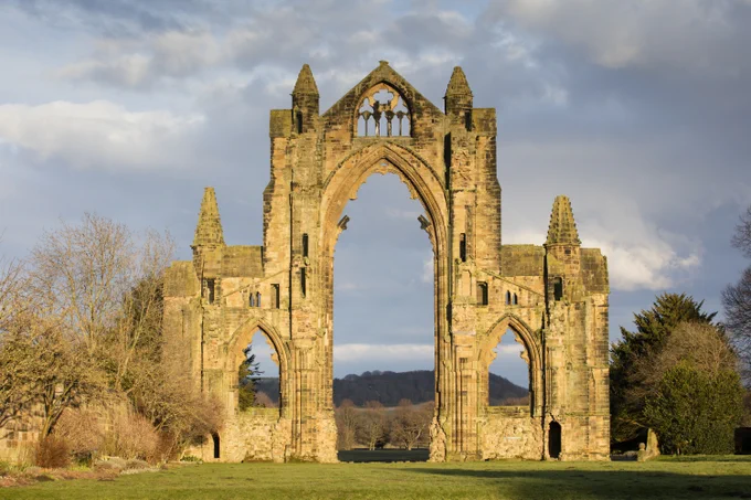 A photograph of the entrance to a ruined abbey surrounded by trees.
