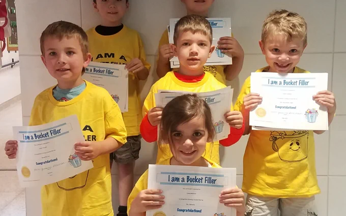 closeup 4 students in matching shirts, smiling and holding certificates