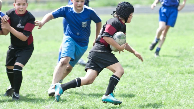 boy plays rugby and runs past opposition players on a bright day on a green pitch